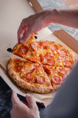 Erkek el, pepperoni pizzasının ilk dilimini teslimat kutusundan çıkarır. Fast food konsepti.