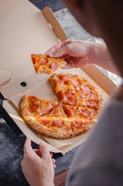 Bir erkek eli pizza kutusundan ısırılmış bir dilim pizza tutar. Fast food konsepti.
