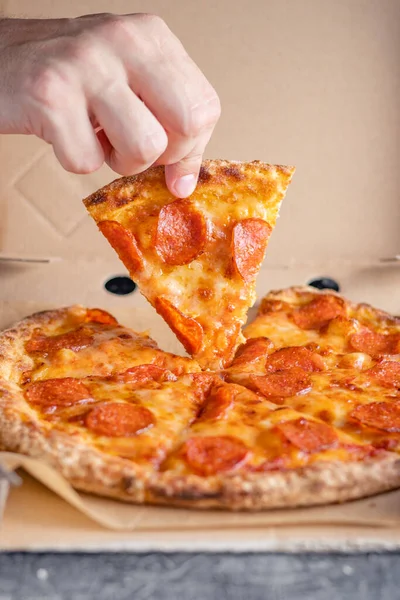 Erkek el, pepperoni pizzasının ilk dilimini teslimat kutusundan çıkarır. Fast food konsepti.