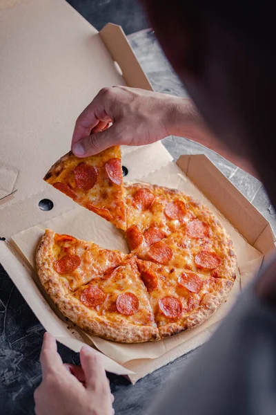 Erkek el, pepperoni pizzasının ilk dilimini teslimat kutusundan çıkarır. Fast food konsepti.