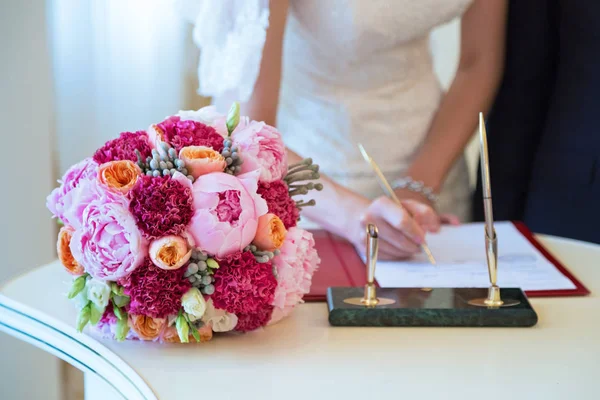 The bride makes a signature on the document, lie next to the document flowers — Stock Photo, Image