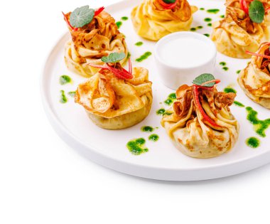 Lezzetli dolgulu, yeşil bitkisel yağ damlaları ve kırmızı biber garnitürlü beyaz bir tabakta servis edilen nefis krep kesesi.