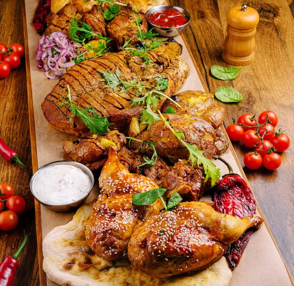 Ahşap bir tahtanın üzerine bol bol kızarmış et serpilir. Yemek, zengin bir sunum için otlar ve taze sebzelerle süslenmiş tavuk, sığır eti ve aromalı kenarları içeriyor..