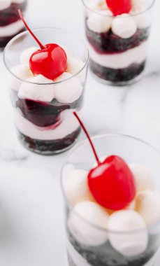 Krema tabakalarıyla dolu lezzetli tatlı fincanları, koyu meyve sosu ve mermer bir yüzeyde düzgünce oturan bir kiraz. Her kutlama ya da toplanma için mükemmel..