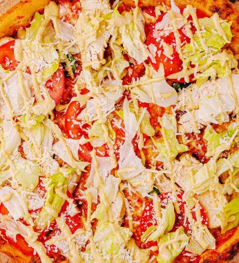 Taze pişmiş pizza, domates, marul ve kremalı sostan oluşan canlı bir karışım içerir. Sıcak kabuk, içerideki doyurucu yemeğin renkli malzemelerini tamamlıyor..