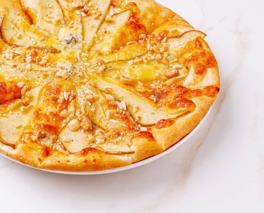 Lezzetli bir pizza, altın kabuklu taze armut dilimleri ve çıtır ceviz içerir. Peynir mükemmel bir şekilde eriyor ve tek başına yemek yemek için ideal bir davet oluşturuyor..