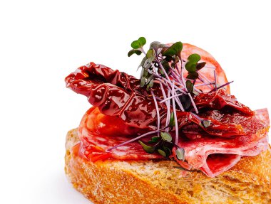 Lezzetli bir bruschetta, üzerinde kurutulmuş et dilimleri, güneşte kurutulmuş domatesler ve bir tutam taze otla lezzetli bir aperatif oluşturan çıtır ekmek içerir..