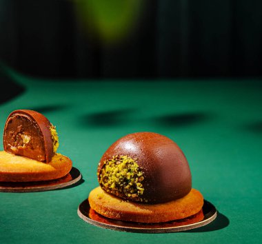 Eşsiz bir çikolatalı tatlı yeşil desenli bir yüzeyde sergilenir. Üzerinde fıstık ezmesi olan yuvarlak bir çikolata küresi ve yanında yumuşak bir pasta tabanı yer alıyor..