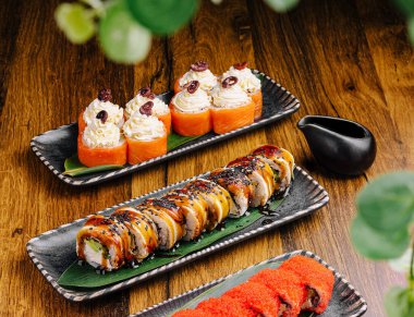 Renkli suşi ruloları balık ve sebze gibi çeşitli malzemelerle uzun tabaklarda sergilenir. Sofrada soslar ve yemek çubukları var, davetkar bir yemek atmosferi yaratıyorlar..
