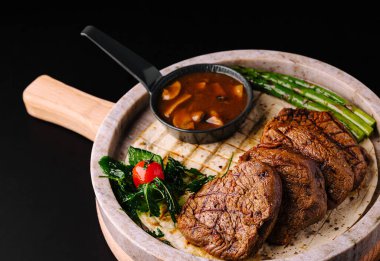 Lezzetli ızgara biftek dilimleri sıcak bir taşın üzerine dizilir. Taze kuşkonmaz ve sotelenmiş yeşillikler ete eşlik eder.