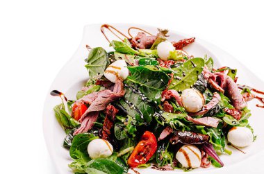 Canlı bir salata sunumunda karışık yeşiller, taze kavrulmuş et, kiraz domatesleri, taze mozzarella topları ve balzamik jöle serpiştirilmiş, hepsi beyaz bir tabakta ustalıkla düzenlenmiş..