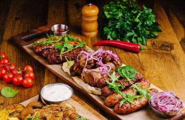 Ahşap bir tabakta çeşitli ızgara etler, soslar, taze otlar ve sebzelerle birlikte. Ziyafette lezzetli dokular, renkler ve baştan çıkarıcı kokular ön plana çıkıyor..