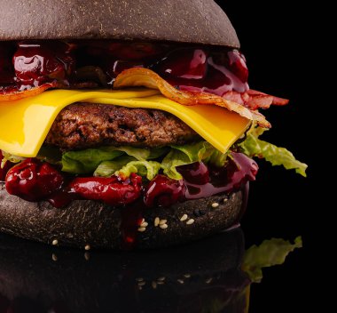 Siyah bir hamburgerde kıtır kıtır pastırma, erimiş peynir, taze marul ve yumuşak susamlı çörek üzerine zengin bir sos bulunur..