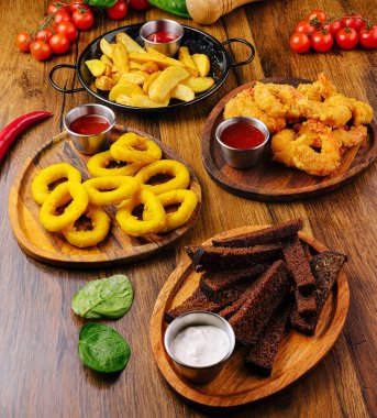 Ahşap tabaklar üzerinde renkli bir çerez çeşidi düzenlenir. Altın soğan halkaları, çıtır çıtır patates kızartmaları ve tuzlu soslar, siyah ekmek ve taze ıspanak..
