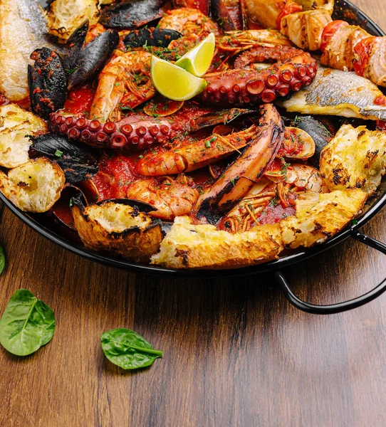 Ahtapot, karides ve çeşitli sebzeler içeren canlı bir deniz ürünleri tabağı ahşap bir masada zarif bir şekilde sergilenir. Yemek kireçle süslenir ve çeşnili kaplarla servis edilir..