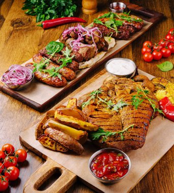 Renkli sebzeler ve olgun domateslerle birlikte taze otlar, soğanlar ve soslarla süslenmiş iki güzel düzenlenmiş tabakta çeşitli ızgara etler yer alıyor..