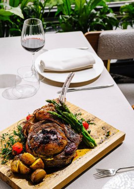Güzel düzenlenmiş bir masa, yanında kuşkonmaz, domates ve kızarmış patatesle birlikte leziz ızgara biftek sunar. Bir bardak kırmızı şarap sofistike atmosferi güçlendirir..