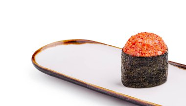 Tek bir parça suşi, parlak beyaz bir tabağın üzerinde duruyor. Suşi, Nori 'ye sarılı zengin, canlı malzemeler içeriyor ve sanatsal bir sunum sergiliyor. Modern mutfak tarzını yansıtıyor..