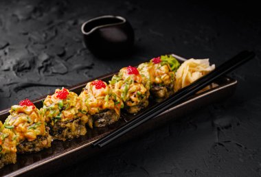 Baharatlı sosla kaplanmış renkli suşi ruloları ve parlak siyah bir tabakta balık yumurtası. Wasabi ve zencefil turşusu eşliğinde, bu yemek tadını çıkarmaya hazır..