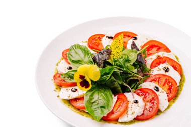 Canlı bir caprese salatasında taze mozzarella ve domates dilimleri, ıspanak ve fesleğen ile güzelce dizilmiş, üzerine bitki sosu serpiştirilmiş ve yenilebilir bir çiçekle süslenmiş..