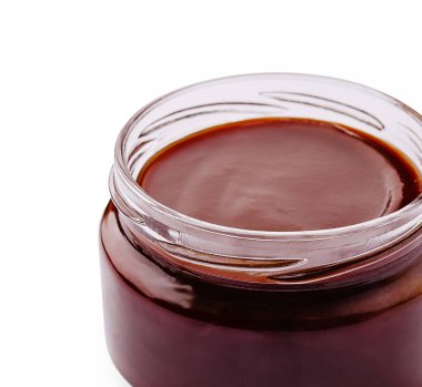 Kalın ve koyu bir sosla dolu cam bir kavanoz temiz, beyaz bir yüzeye oturur. Sos, çeşitli mutfak kullanımları için hazır, zengin bir dokuya sahip parlak görünüyor..