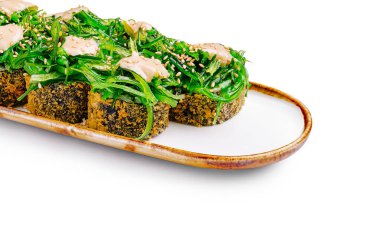 Renkli suşi dürümleri, taze yeşil deniz yosunlarıyla süslenmiş ve kremalı sosla süslenmiş uzun bir tabağa konur. Sıradan bir öğle yemeği ya da yemek deneyimi için ideal..