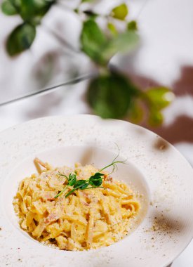 Taze otlarla kaplı lezzetli bir kremalı makarna tabakta zarif bir şekilde duruyor. Restoranın atmosferinde hoş bir yeşillik var, rahat bir yemek deneyimi yaratıyor..