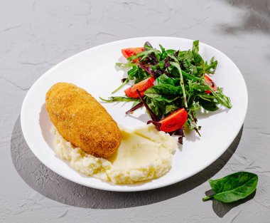 Altın bir kroket kremalı patates püresi ve taze domates ve yeşilliklerle kaplı canlı bir salatanın yanında oturur. Bu lezzetli yemek, öğle yemeğinde tatminkar bir yemek için mükemmel..