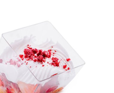 Taze çilek parçaları ve kırıntılarla kaplı kremalı tatlı dolu berrak bir fincan. İkram, tatlı bir hoşgörüyü davet eden zengin, yumuşak bir dokuya sahip..