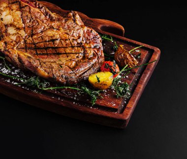 Renkli sebzelerle süslenmiş güzel pişmiş bir biftek ahşap bir tahtanın üzerinde dinleniyor. Dekor etin zengin, kömürleşmiş dokusunu vurguluyor, bir gurme yemek deneyimini vurguluyor.