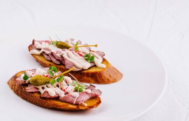 Et soslu ve kapari soslu iki lezzetli bruschetta beyaz bir tabakta yatıyor.