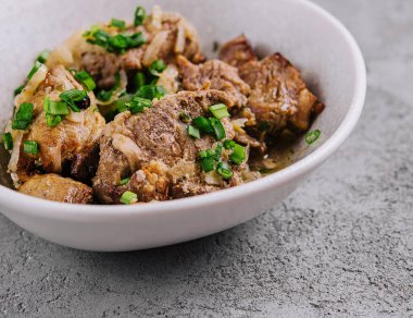 Beyazlar içinde yeşil soğan ile süslenmiş ağır ateşte pişirilmiş et parçaları servis edilmeye hazır.