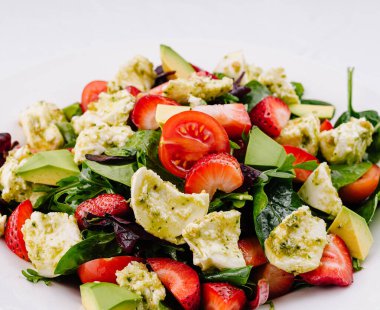 Dilimlenmiş çilek, avokado ve peynirli canlı yeşil salata.
