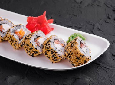 White plate with sushi rolls, ginger, and wasabi on a textured black surface