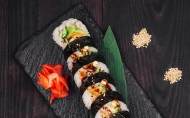 Lezzetli taze hazırlanmış suşi ruloları somon, avokado ve siyah tabakta servis edilen susam tohumları.