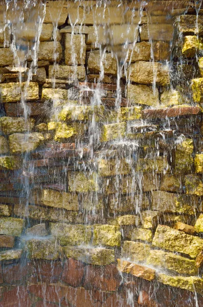 Water flows through the stone wall.It is a beautiful miniature waterfall.