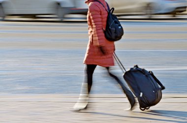 Kızı uçağa koşar. Tekerlek üzerinde büyük bir bavul var. O onun arkasında rulo.