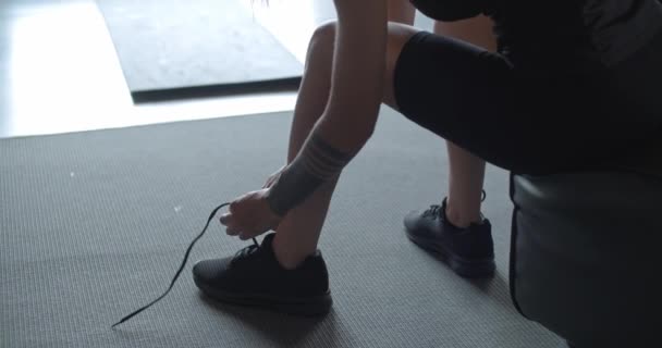 Tatuado mulher amarrando seus sapatos antes de fitness treino desportivo em casa. Pernas e sapatos detalhe. .Sala de estar treinamento doméstico. 4k câmera lenta de vídeo — Vídeo de Stock