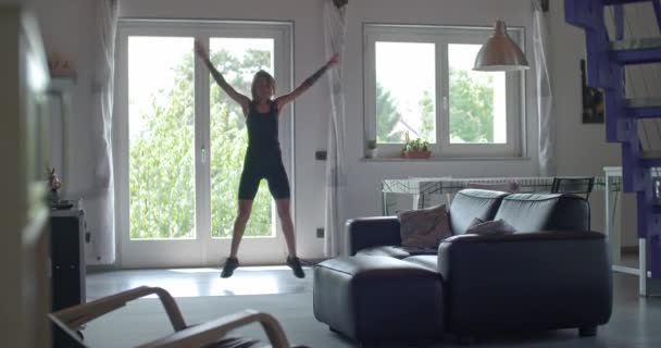 Junge tätowierte Frau beim Jumping Jack-Training während des Heimfitnesstrainings im Wohnzimmer. 4k Zeitlupenvideo — Stockvideo