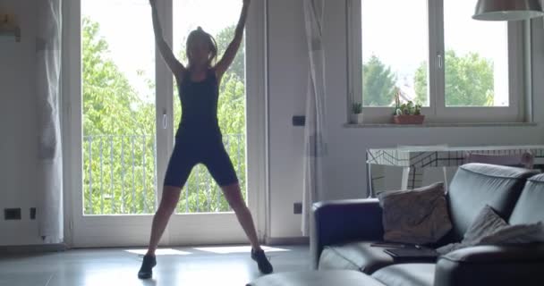 Молодая татуированная женщина делает прыжки валеты упражнения во время домашнего фитнеса спортивные тренировки. 4к замедленное видео — стоковое видео