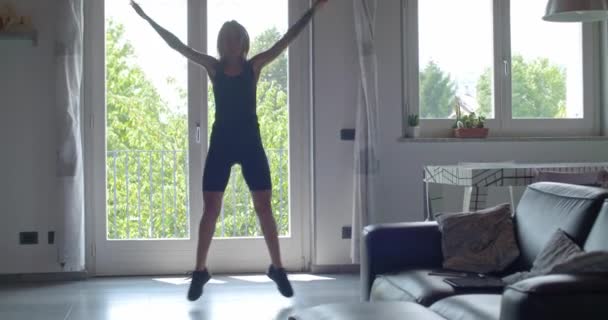 Junge tätowierte Frau beim Jumping Jack-Training während des Heimfitnesstrainings im Wohnzimmer. 4k Zeitlupenvideo — Stockvideo