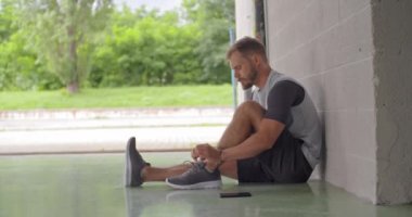 Fitness Spor egzersiz için hazırlanıyor genç yetişkin adam kravat Ayakkabı bağcıklarımı oturmuş. Yan görünümü. Grunge endüstriyel kentsel training.4k ağır çekim video