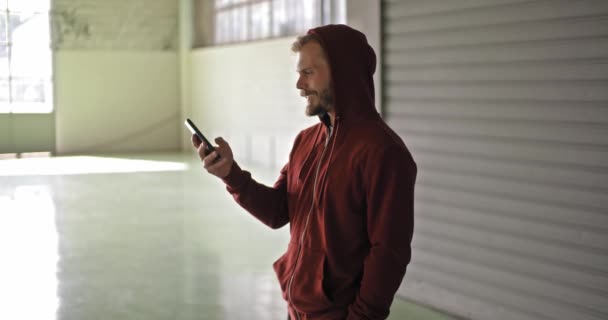 Jonge volwassen man met hooded sweatshirt met smartphone tijdens sport fitnesstraining. Grunge industriële stedelijke training.4k slowmotion video — Stockvideo