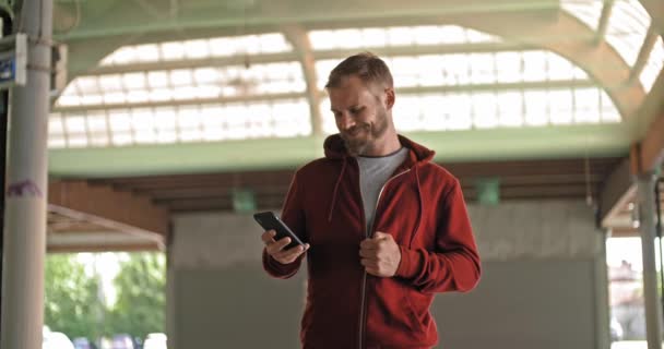 Hombre adulto joven con sudadera con capucha usando teléfono inteligente durante el entrenamiento deportivo de fitness. Grunge entrenamiento urbano industrial. — Vídeos de Stock