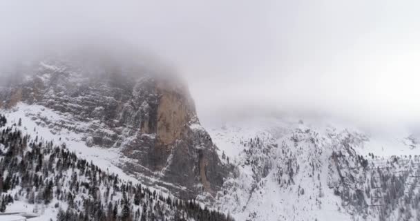 Aérea hacia atrás con montaña nevada y bosque de bosques en Sella pass.Nublado mal nublado niebla weather.Winter Dolomites montañas de los Alpes italianos naturaleza al aire libre establishment. — Vídeo de stock