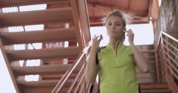 Młoda blond kobieta w fitness nosić schodząc po schodach ocieplenie się systemem szkolenia. Słoneczny letni dzień. Zielone miasto przemysłowe. Miejskiego biegacza cardio zdrowej aktywności workout.4k wideo w zwolnionym tempie 60p — Wideo stockowe