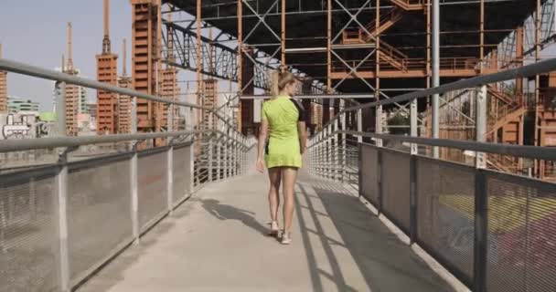 Νεαρή ξανθιά γυναίκα στο φορούν γυμναστήριο ζέσταμα στη διάβαση πεζών για την εκτέλεση του κατάρτιση. Ηλιόλουστη μέρα του καλοκαιριού. Πράσινη βιομηχανική πόλη. Αστικό δρομέα καρδιο υγιή δραστηριότητα workout.4k αργή κίνηση 60p βίντεο — Αρχείο Βίντεο