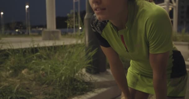 Müde Frau in Fitnessbekleidung, die sich nach dem Training ausruht. Seitenansicht.Sommerabend oder Nacht.Industrial Green City.Urban Runner Cardio gesundes Aktivitätstraining .4k Zeitlupe 60p Video — Stockvideo