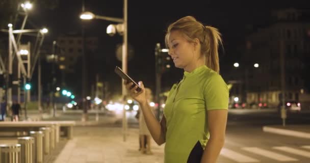 Femme fatiguée dans l'usure de remise en forme à l'aide d'un smartphone après l'entraînement.vue rapprochée du visage.Soirée d'été ou nuit. ville verte industrielle. cardio coureur urbain entraînement d'activité saine.4k ralenti 60p vidéo — Video