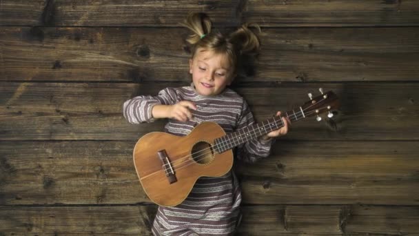 Ragazza felice bambino sopraelevato su sfondo vintage in legno giocare ukulele chitarra.Testo o logo copia spazio.Verticale vista dall'alto. — Video Stock